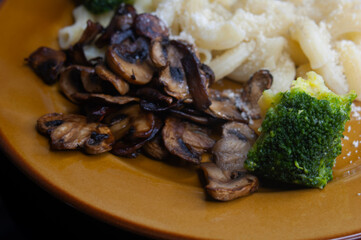 close up of roasted mushrooms with brocolli and pasta on a brown plate 