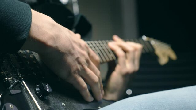Close up fingers of guitarist at the strings. Mens arms plays solo of rock music. Hands of male musician playing at electric guitar. Beautiful black background at studio. Slow motion Close up