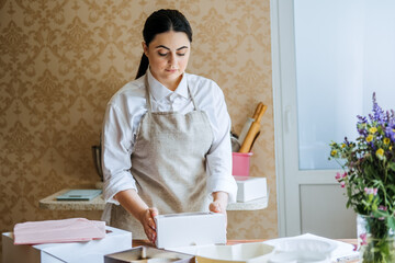 Female baker, pastry chef preparing cake order. Arabic Asian woman making cake for online delivery