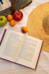 book, straw hat and some pieces of fruit of apples and apricot on the beach