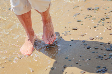 Elderly woman's feet walking on the sand on the beach