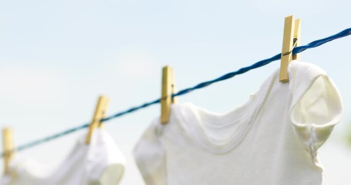 White baby clothes hanging on rope outdoors on spring day
