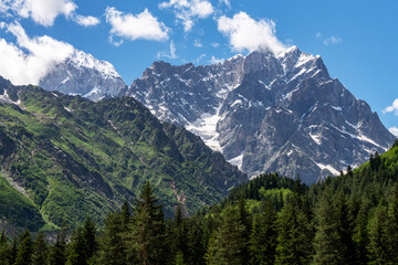 Beautiful alpian mountains landscape. High snow covered mountains green high forset on the hills under blue sky with clouds.