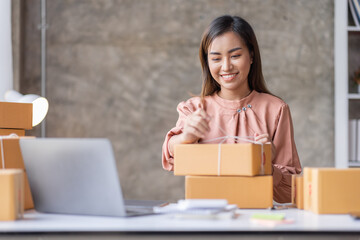 SME Online seller Young Asian woman working on laptop and box checking online order, check goods stock delivery package shipping postal. Asian woman startup SME small business at home office