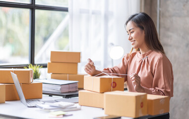 Obraz na płótnie Canvas SME Online seller Young Asian woman working on laptop and box checking online order, check goods stock delivery package shipping postal. Asian woman startup SME small business at home office
