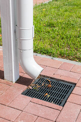 A white rainwater drain pipe and a drainage system with a grate built into the paving slabs.