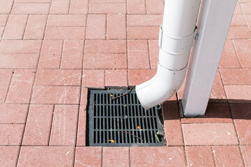 A white rainwater drain pipe and a drainage system with a grate built into the paving slabs.