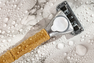 Men's razor on a marble table in the rays of the morning sun and drops of water, shaving foam