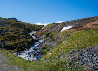 Hill with stream, grass, snow and stones