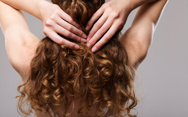 Fototapeta premium a woman with long well-groomed curly hair stands on a gray background and demonstrates them