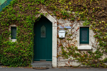 Door with triangle shape door wall with overgrown green foliage and two small window and post box. Old style home residence.