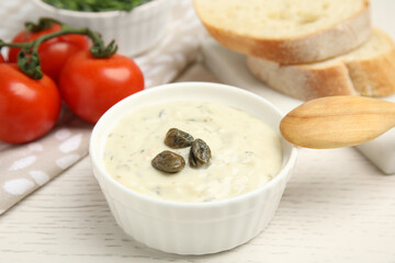 Creamy caper sauce in bowl on white wooden table, closeup