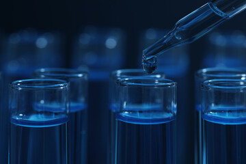 Dripping reagent into test tube with blue liquid on dark background, closeup. Laboratory analysis