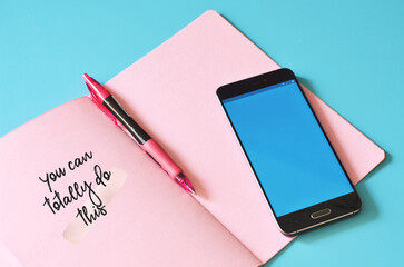 Smartphone and pink notebook with text You can do this on blue table. Mock up for design