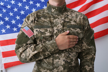 Soldier holding hand on heart near United states of America flag on white background, closeup