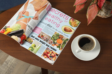 Open magazine, cup of coffee and houseplant on wooden table indoors, above view