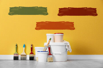 Decorator's tools on wooden floor near white wall with samples of different paints indoors