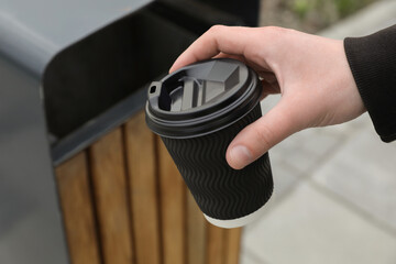Man throwing black paper cup into trash can outdoors, closeup