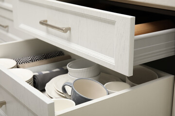 Fototapeta na wymiar Open drawers of kitchen cabinet with different dishware and towels