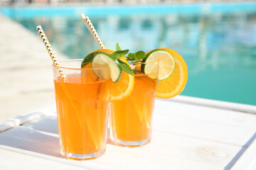 Refreshing cocktail in glasses near outdoor swimming pool on sunny day