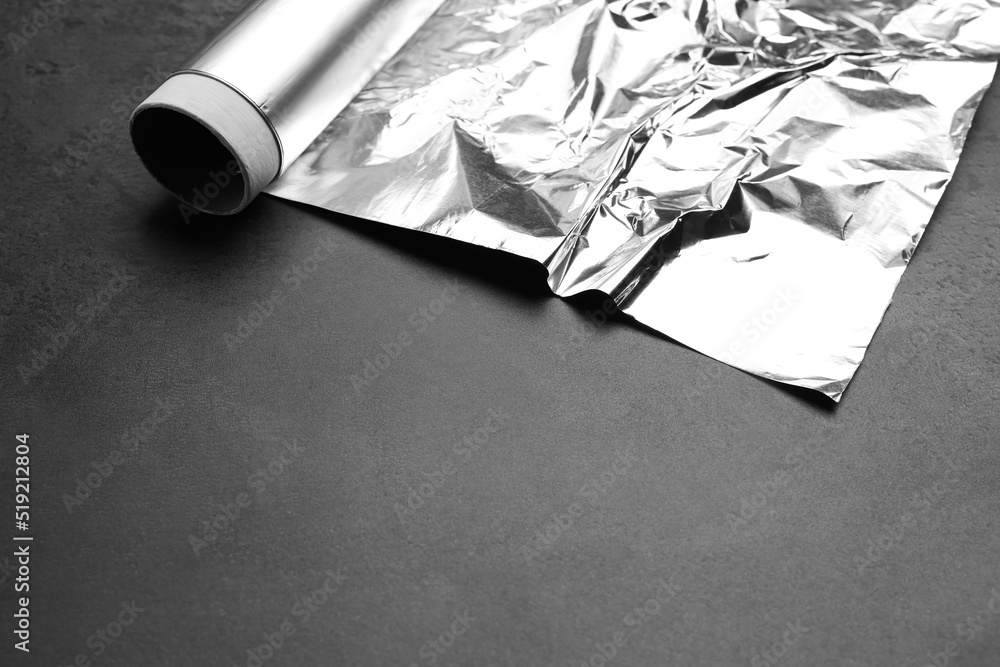 Wall mural Roll of aluminum foil on grey dark table, closeup. Space for text