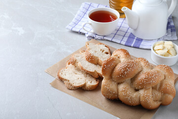 Cut homemade braided bread and freshly brewed tea on light grey table, space for text. Traditional...