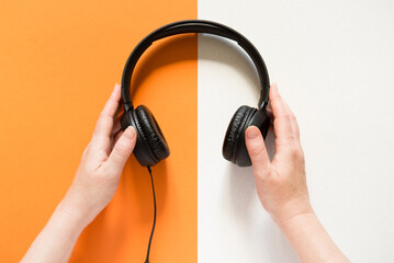 Hands holding headphones on a bicolor orange and white background. view from above. copy space