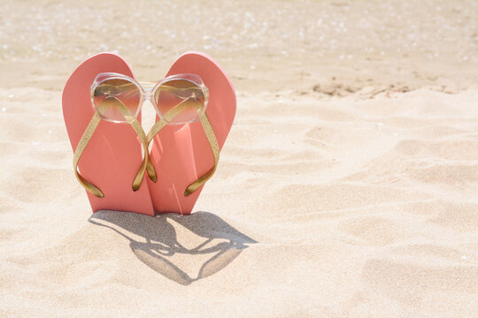 Stylish pink flip flops with sunglasses in sand on sunny day, space for text