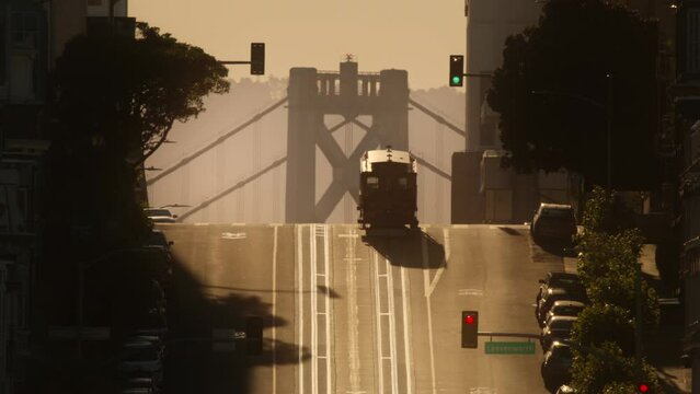 California street district in San Francisco, USA with historic tram riding up hill with Bay Bridge on background. RED camera shot of San Francisco hills on golden hour with cinematic morning sunlight