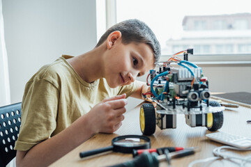 Concentrated boy building electronic robot while looking attentively on it at home. Education,...