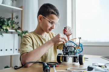 Child boy assembling in robotics class in the classroom. Concentrated focused boy in glasses having fun in workshop. Inventive kid enjoying science lesson at school
