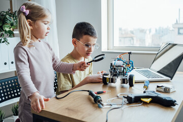 Little sister helping to her brother working on handmade robotic car model. Concentrated boy creating robot at lab. Early development, diy, innovation, modern technology concept