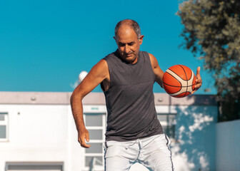 Portrait of Turkish Cypriot elderly athletic man playing basketball outdoor at summer sunny day