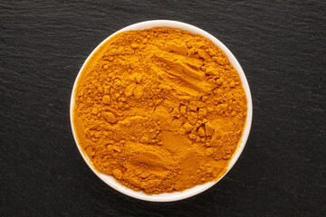 Aromatic seasoning turmeric in a white ceramic dish on a slate stone, close-up, top view.