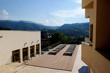 View of a wooden brown terrace with empty beds and the green mountain forest in the background.