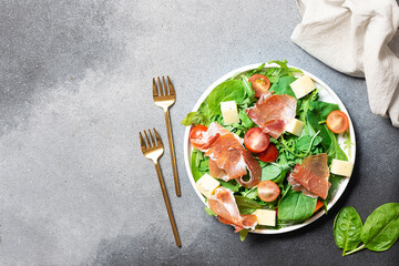 Fresh juicy green salad with cherry tomatoes, goat cheese and prosciutto on black stone background...