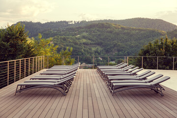 View of a wooden brown terrace with empty beds and the green mountain forest in the background.