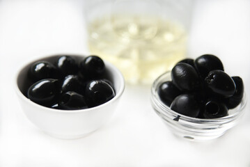 Black olives in a saucepan and olive oil on a white background.