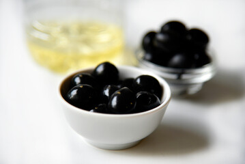 Black olives in a saucepan and olive oil on a white background.