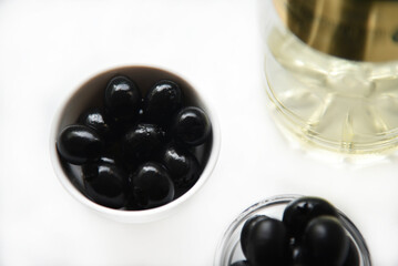 Black olives in a saucepan and olive oil on a white background.