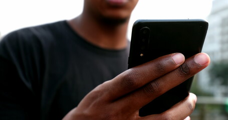 Mixed race man using smartphone in street. African black guy holding cellphone browsing