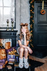 Fototapeta premium A girl with white hair is sitting on the floor near a Christmas tree and a box of gifts