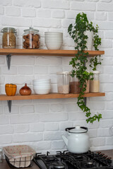 Wooden shelves with glass jars with cookies, pasta, cereals. There is kettle on the stove. Selective focus. Image for articles about cooking, food, kitchens.