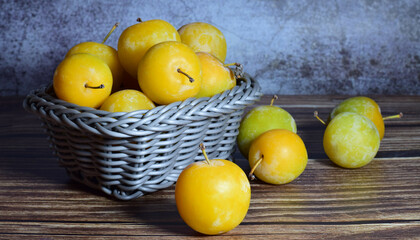 Close up, yellow plum and group on wicker basket. Wooden base stone background. Front shot and copy space.