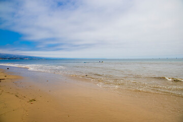 surfers riding the waves in vast blue ocean water with blue sky and clouds at Leadbetter Beach in Santa Barbara California USA
