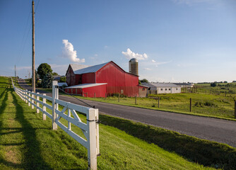 Amish farm with a red barn beside a country road and white fence on a sunny summer day in Holmes County, Ohio