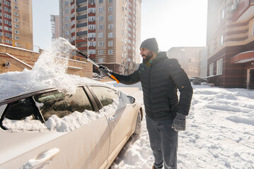 A young man cleans his car after a snowfall on a sunny, frosty day. Cleaning and clearing the car...