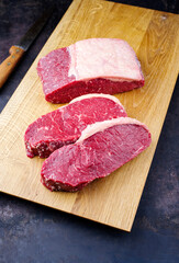 Raw dry aged wagyu roast beef steak offered as close-up on a wooden design board