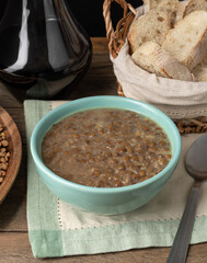 Brown lentil soup in a bowl with bread slices and wine over wooden table