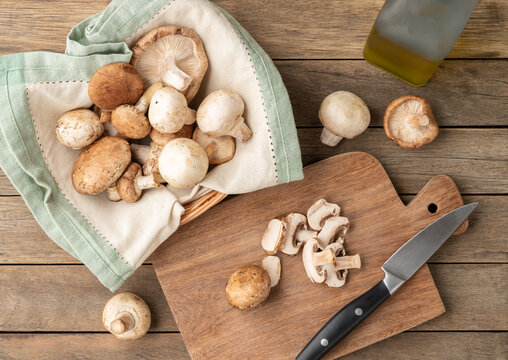 Shitake, portobello and paris mushrooms in a basket with slices over wooden board